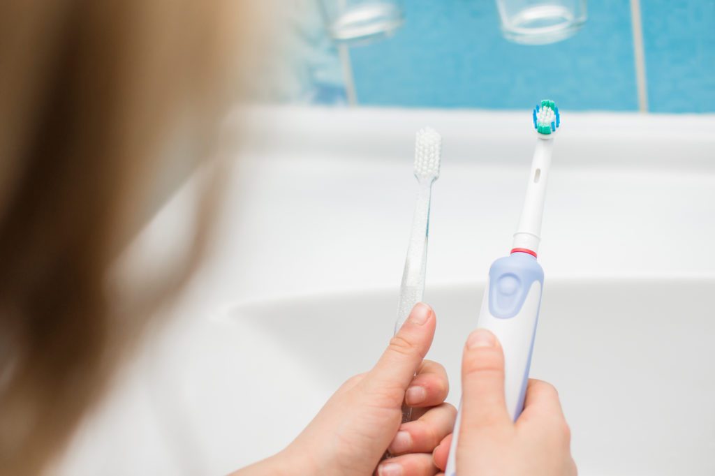 A patient at Tri-City Dental considers a manual toothbrush and an electric toothbrush